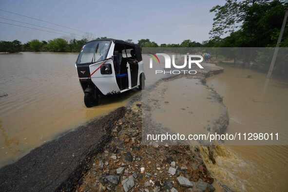 People are riding three-wheelers on a road damaged by flood following rains in the aftermath of Cyclone Remal, in Nagaon district of Assam,...