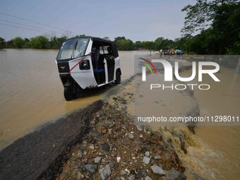 People are riding three-wheelers on a road damaged by flood following rains in the aftermath of Cyclone Remal, in Nagaon district of Assam,...