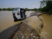 People are riding three-wheelers on a road damaged by flood following rains in the aftermath of Cyclone Remal, in Nagaon district of Assam,...