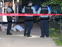 Chicago Police are canvassing the area for evidence as a male victim who was shot twenty-five times and killed is covered with a sheet. A ma...