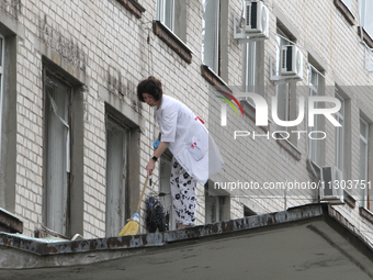 A healthcare worker is sweeping away glass shards from the roof of a portico at a hospital damaged by the falling debris of downed Russian m...