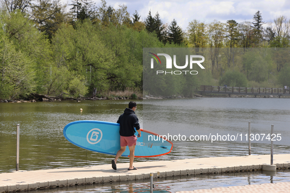 A man is carrying a paddleboard along Lake Wilcox in Richmond Hill, Ontario, Canada, on May 12, 2024. 