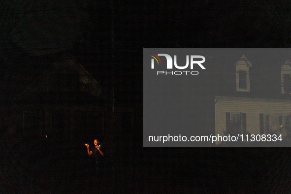 A news reporter is illuminated by a camera light in a dark Gaithersburg, Maryland neighborhood on June 5, 2024, after a tornado swept throug...