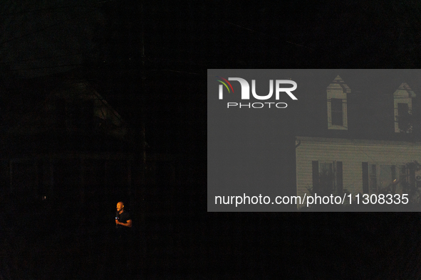 A news reporter is illuminated by a camera light in a dark Gaithersburg, Maryland neighborhood on June 5, 2024, after a tornado swept throug...