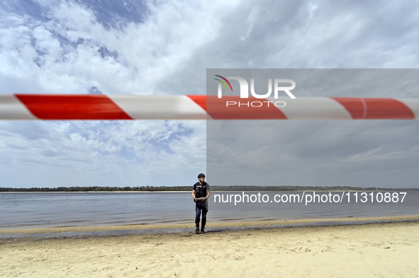 An EOD expert is holding a bomb on the Dnipro River bank behind red and white caution tape during the training of State Emergency Service pe...