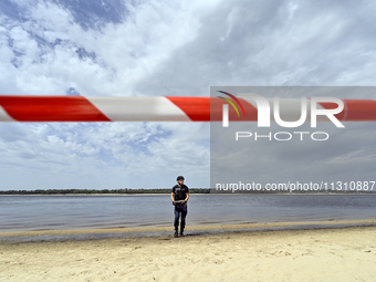 An EOD expert is holding a bomb on the Dnipro River bank behind red and white caution tape during the training of State Emergency Service pe...