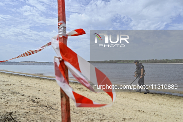 An EOD expert is scanning the Dnipro River bank with a metal detector behind red and white caution tape during the training of State Emergen...