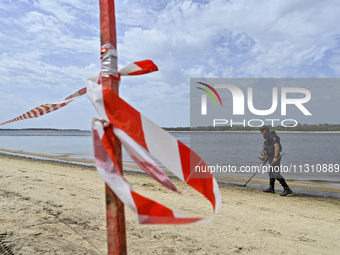 An EOD expert is scanning the Dnipro River bank with a metal detector behind red and white caution tape during the training of State Emergen...