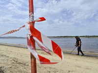 An EOD expert is scanning the Dnipro River bank with a metal detector behind red and white caution tape during the training of State Emergen...