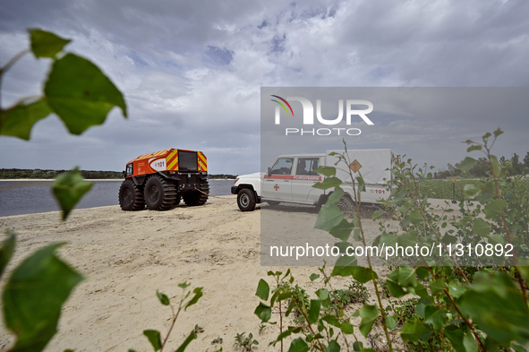 A Bohun-2 snowmobile is towing an SES vehicle, which is unable to reach the site of an explosive device due to sandy soil and a flooded floo...