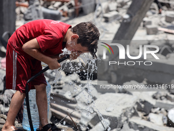 A Palestinian boy is pouring water over himself amidst a heatwave a day after an operation by the Israeli Special Forces in the Nuseirat cam...