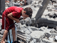 A Palestinian boy is pouring water over himself amidst a heatwave a day after an operation by the Israeli Special Forces in the Nuseirat cam...