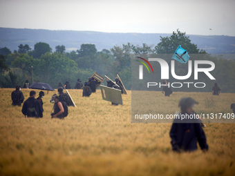 A black bloc is standing in a wheat field with the flag of the 'Soulevements de la Terre' (i.e., 'Earth Uprisings'). Nearly 5,000 people are...