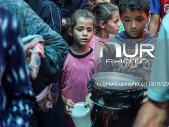 Palestinians are queuing for meal rations at a communal food distribution point in Deir al-Balah in the besieged Gaza Strip on June 10, 2024...