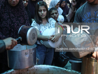 Palestinians are queuing for meal rations at a communal food distribution point in Deir al-Balah in the besieged Gaza Strip on June 10, 2024...