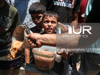 Palestinians are queuing for meal rations at a communal food distribution point in Deir al-Balah in the besieged Gaza Strip on June 10, 2024...