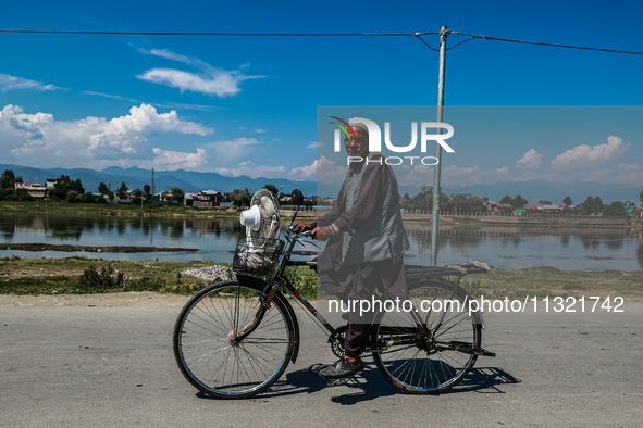 An elderly man is carrying a fan on his bicycle on a hot summer day in Sopore, Baramulla, Jammu and Kashmir, India, on June 11, 2024. 