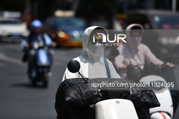 Citizens are wearing sun-protective clothing and riding on a street under high temperatures in Fuyang, China, on June 12, 2024. The Central...