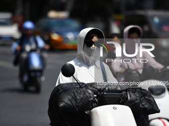 Citizens are wearing sun-protective clothing and riding on a street under high temperatures in Fuyang, China, on June 12, 2024. The Central...