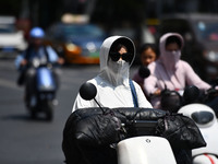 Citizens are wearing sun-protective clothing and riding on a street under high temperatures in Fuyang, China, on June 12, 2024. The Central...