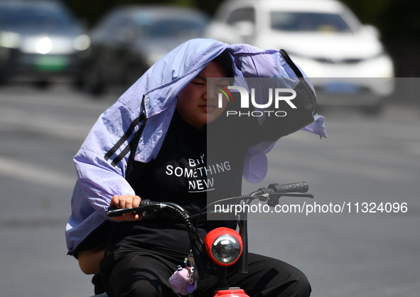 Citizens are wearing sun-protective clothing and riding on a street under high temperatures in Fuyang, China, on June 12, 2024. The Central...