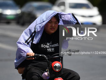 Citizens are wearing sun-protective clothing and riding on a street under high temperatures in Fuyang, China, on June 12, 2024. The Central...