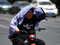 Citizens are wearing sun-protective clothing and riding on a street under high temperatures in Fuyang, China, on June 12, 2024. The Central...