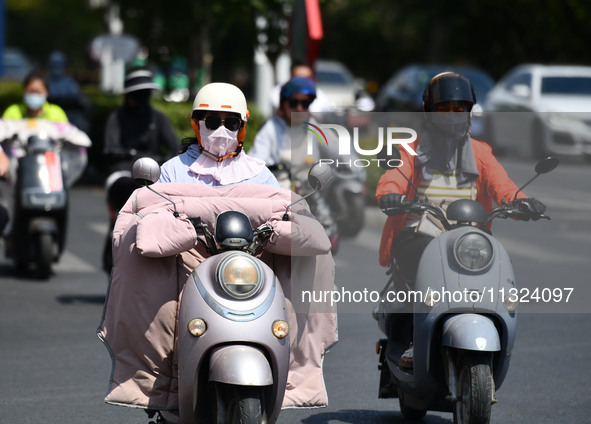 Citizens are wearing sun-protective clothing and riding on a street under high temperatures in Fuyang, China, on June 12, 2024. The Central...