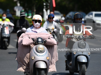 Citizens are wearing sun-protective clothing and riding on a street under high temperatures in Fuyang, China, on June 12, 2024. The Central...