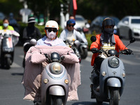 Citizens are wearing sun-protective clothing and riding on a street under high temperatures in Fuyang, China, on June 12, 2024. The Central...