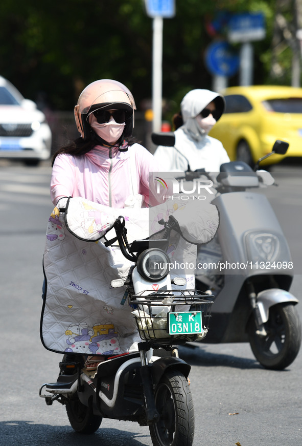 Citizens are wearing sun-protective clothing and riding on a street under high temperatures in Fuyang, China, on June 12, 2024. The Central...