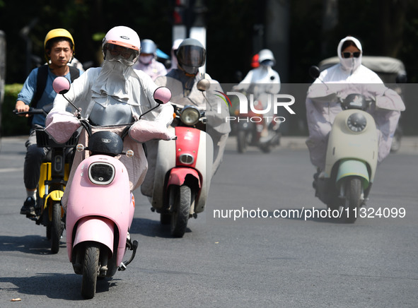 Citizens are wearing sun-protective clothing and riding on a street under high temperatures in Fuyang, China, on June 12, 2024. The Central...