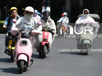 Citizens are wearing sun-protective clothing and riding on a street under high temperatures in Fuyang, China, on June 12, 2024. The Central...