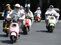 Citizens are wearing sun-protective clothing and riding on a street under high temperatures in Fuyang, China, on June 12, 2024. The Central...