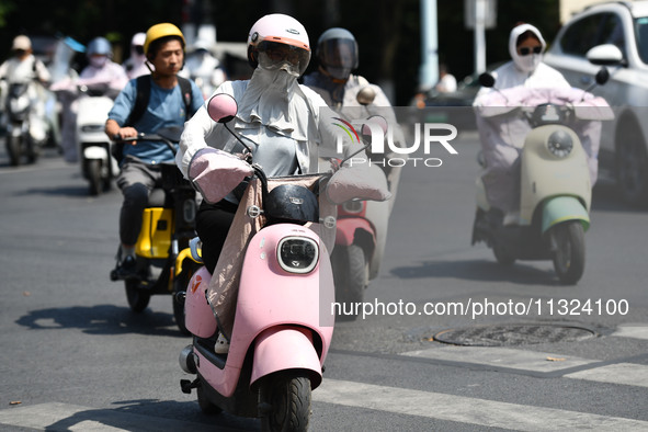 Citizens are wearing sun-protective clothing and riding on a street under high temperatures in Fuyang, China, on June 12, 2024. The Central...