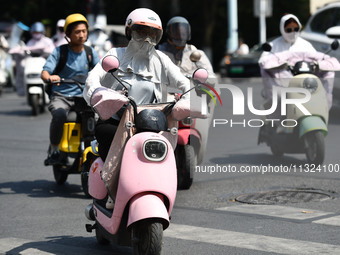 Citizens are wearing sun-protective clothing and riding on a street under high temperatures in Fuyang, China, on June 12, 2024. The Central...