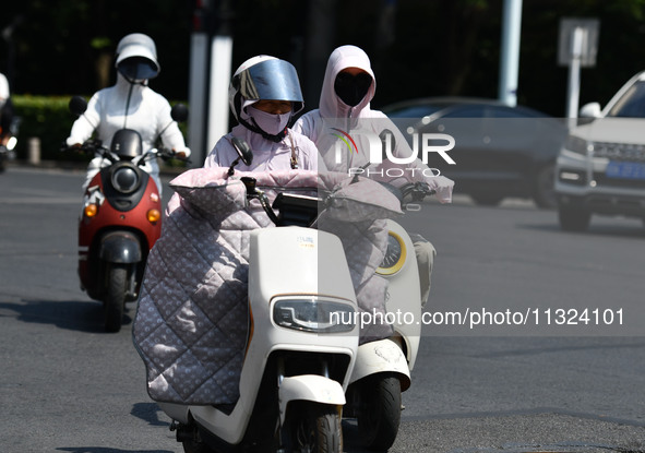 Citizens are wearing sun-protective clothing and riding on a street under high temperatures in Fuyang, China, on June 12, 2024. The Central...