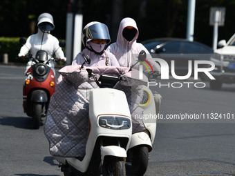 Citizens are wearing sun-protective clothing and riding on a street under high temperatures in Fuyang, China, on June 12, 2024. The Central...