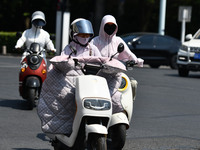 Citizens are wearing sun-protective clothing and riding on a street under high temperatures in Fuyang, China, on June 12, 2024. The Central...