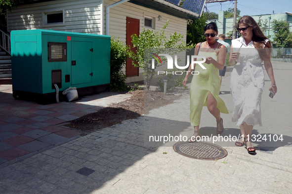 Two women are walking past a generator powering a cafe at the seaside during rolling blackouts in Odesa, Ukraine, on June 11, 2024. NO USE R...