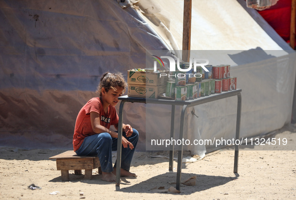 A displaced girl is selling preserves and waiting for customers on a street next to tents in Deir el-Balah, in the central Gaza Strip, on Ju...