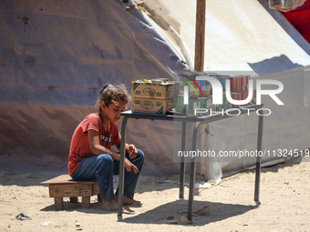 A displaced girl is selling preserves and waiting for customers on a street next to tents in Deir el-Balah, in the central Gaza Strip, on Ju...