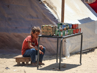 A displaced girl is selling preserves and waiting for customers on a street next to tents in Deir el-Balah, in the central Gaza Strip, on Ju...