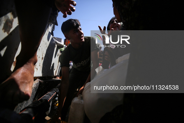 Palestinians are lining up to fill their containers with water on a street next to tents in Deir el-Balah, in the central Gaza Strip, on Jun...