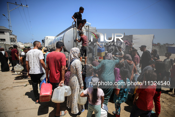 Palestinians are lining up to fill their containers with water on a street next to tents in Deir el-Balah, in the central Gaza Strip, on Jun...