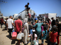 Palestinians are lining up to fill their containers with water on a street next to tents in Deir el-Balah, in the central Gaza Strip, on Jun...