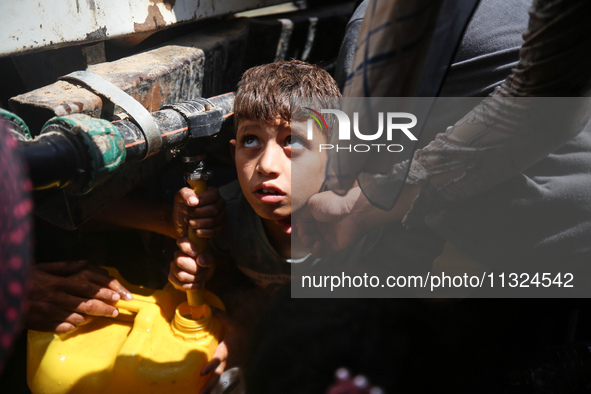 Palestinians are lining up to fill their containers with water on a street next to tents in Deir el-Balah, in the central Gaza Strip, on Jun...