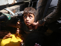 Palestinians are lining up to fill their containers with water on a street next to tents in Deir el-Balah, in the central Gaza Strip, on Jun...