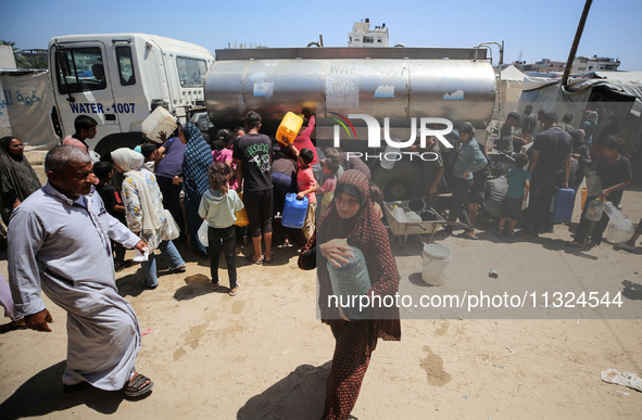 Palestinians are lining up to fill their containers with water on a street next to tents in Deir el-Balah, in the central Gaza Strip, on Jun...