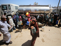 Palestinians are lining up to fill their containers with water on a street next to tents in Deir el-Balah, in the central Gaza Strip, on Jun...